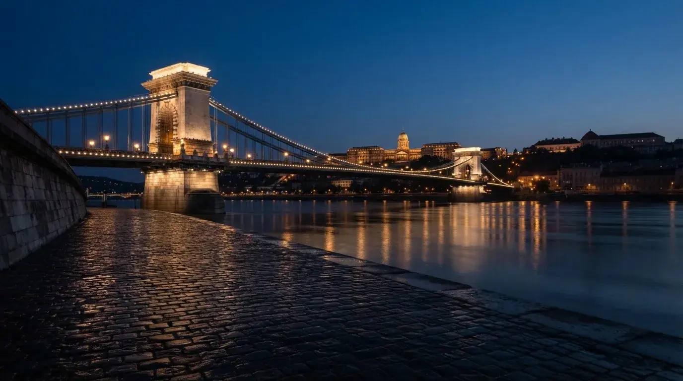 A budapesti Lánchíd esti fényekben a Duna fölött, a háttérben a budai Vár, forgalom nélküli rakpart.