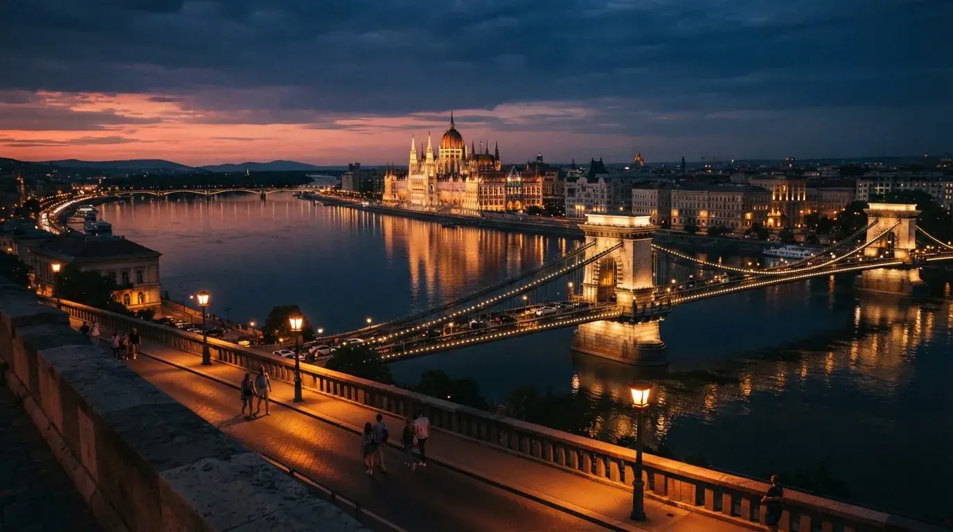 Budapesti belváros esti látképe a Duna-parttal és a Parlament sziluettjével, járókelők a rakparton, megvilágított hivatali épületek.